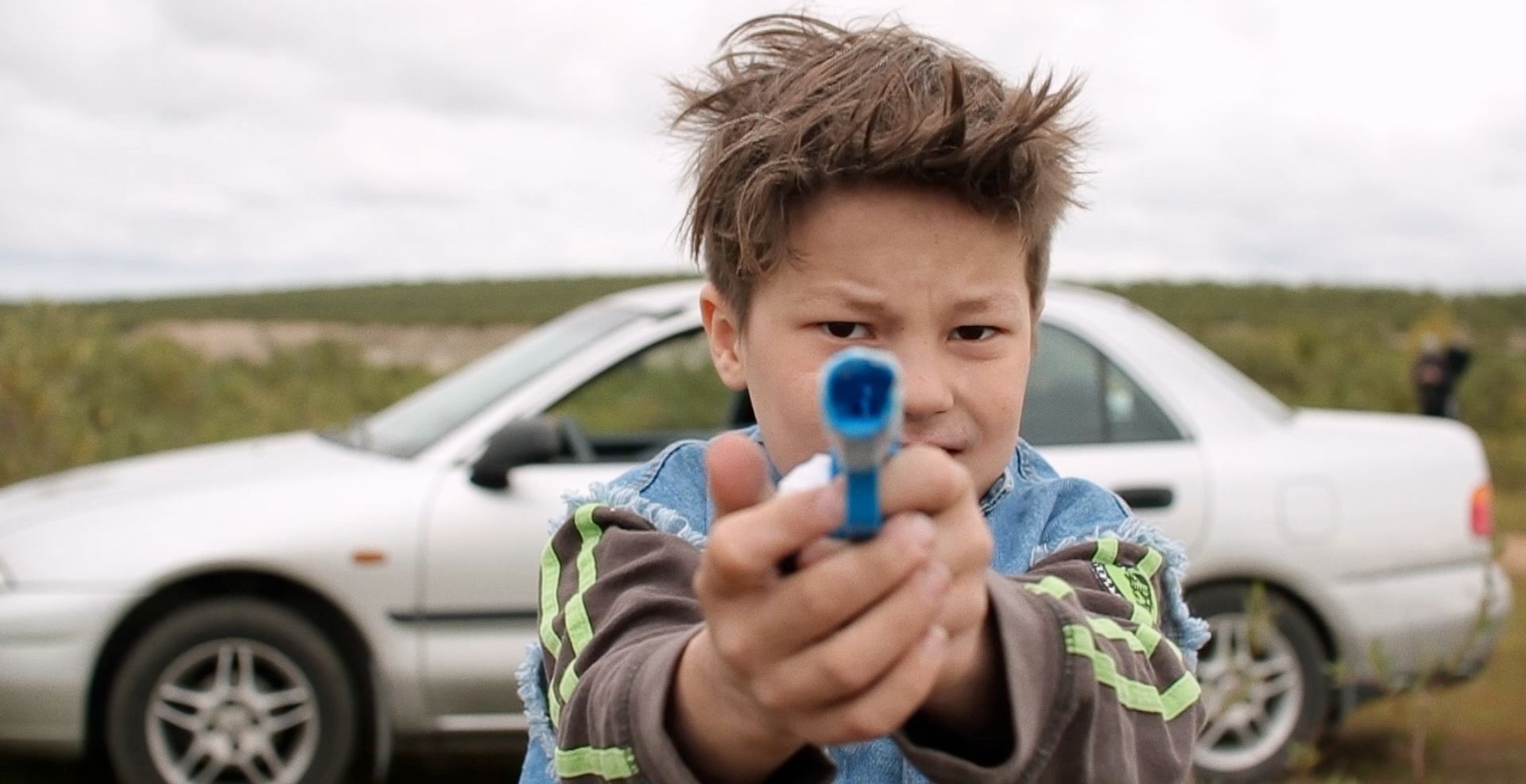 A Kid in Norway aims at the camera with a plastic pistol