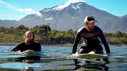 two surfers paddle down the ocean while in their wetsuits