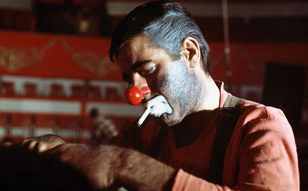 a clown with a well-groomed red nose smokes a cigarette