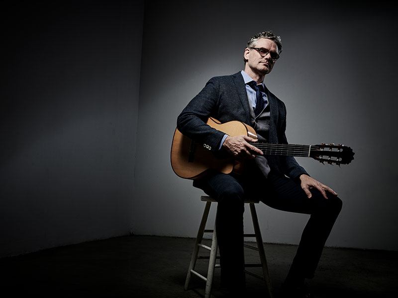 a guitarist with white hair and glasses poses with his guitar