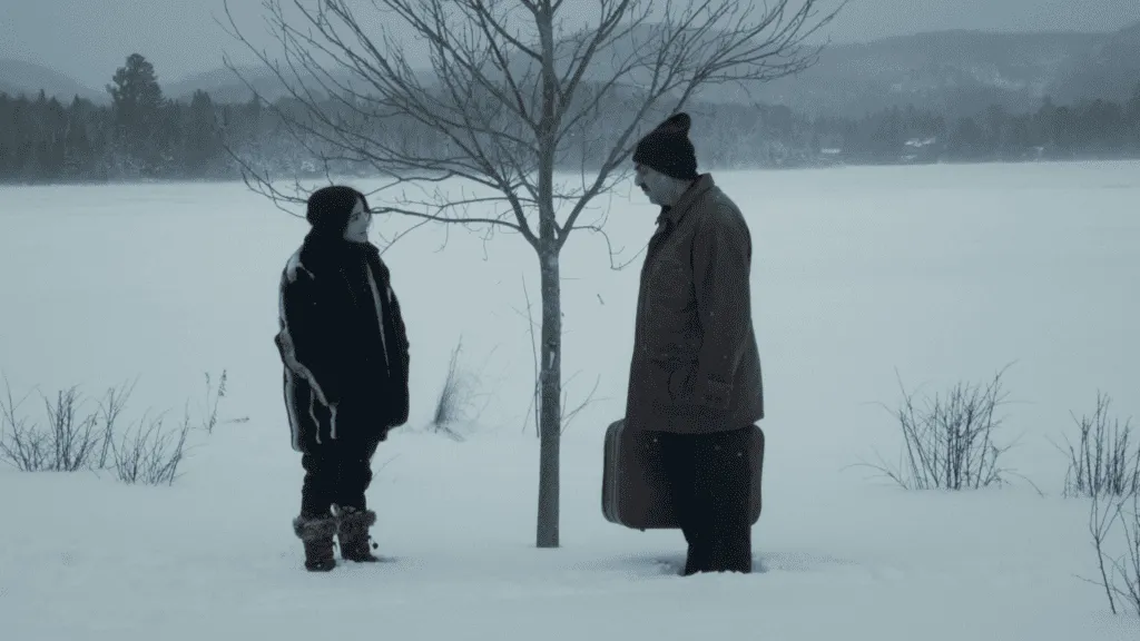 A girl in a black sweater looks at a man carrying a suitcase. They're in a snowy landscape.