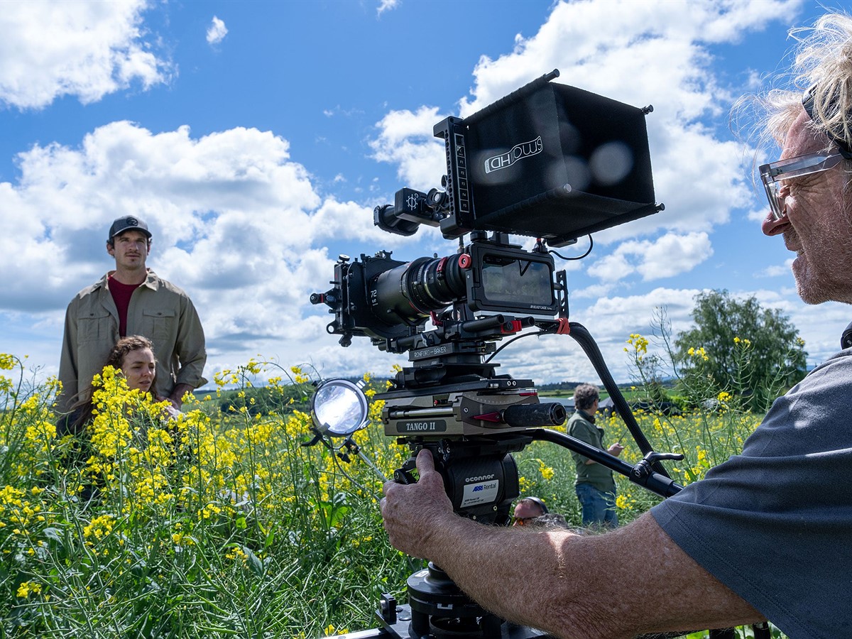 among yellow flowers a director with his camera recording and a couple among the flowers.