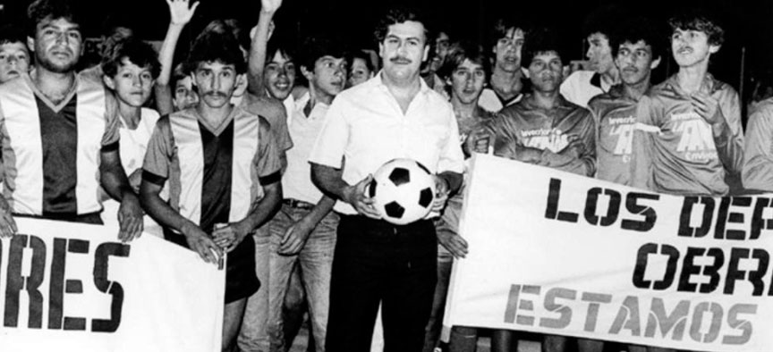 A group of soccer players in uniform and a man in a shirt and mustache