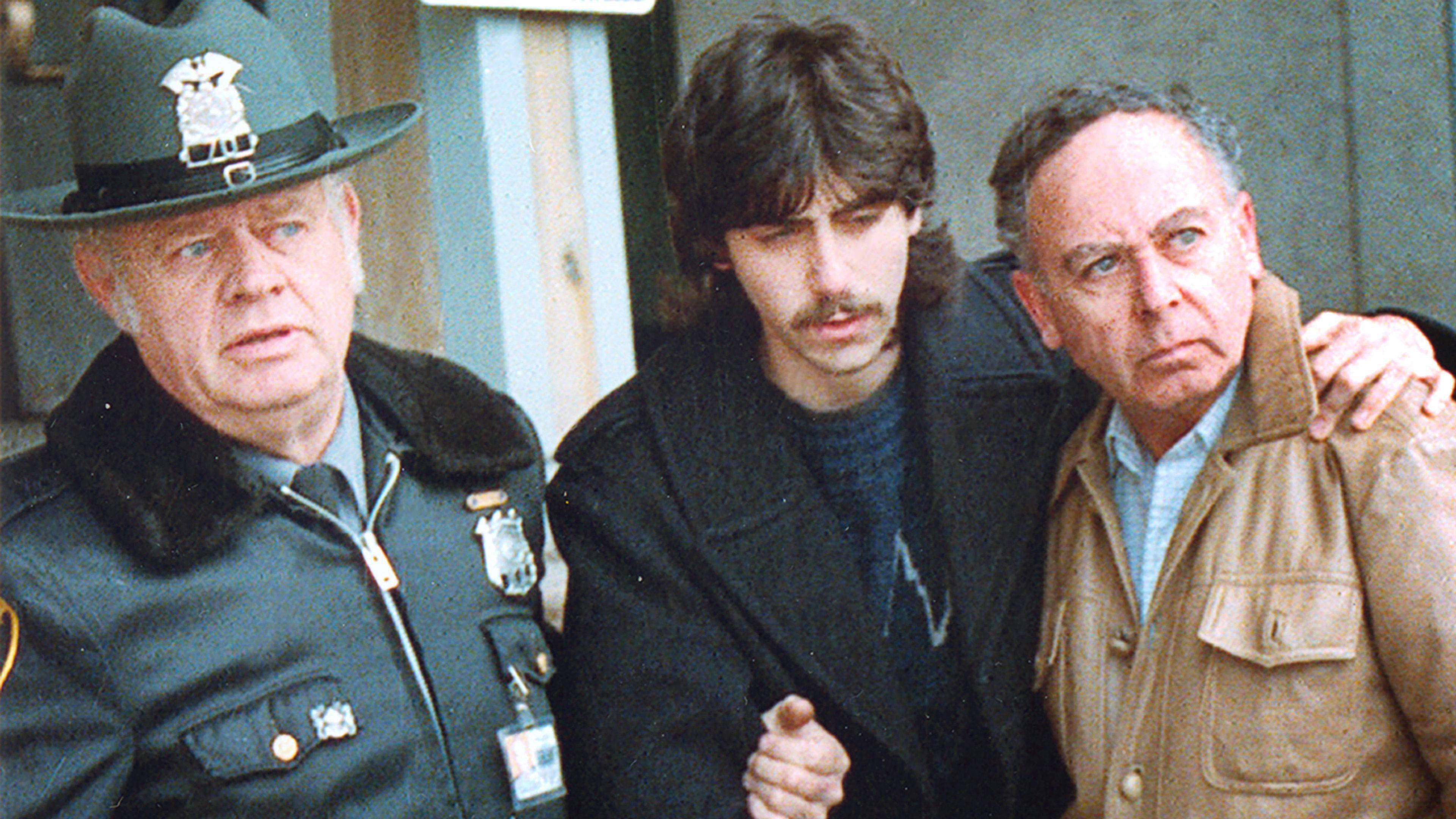 Two policemen in hats take away an arrested bearded man