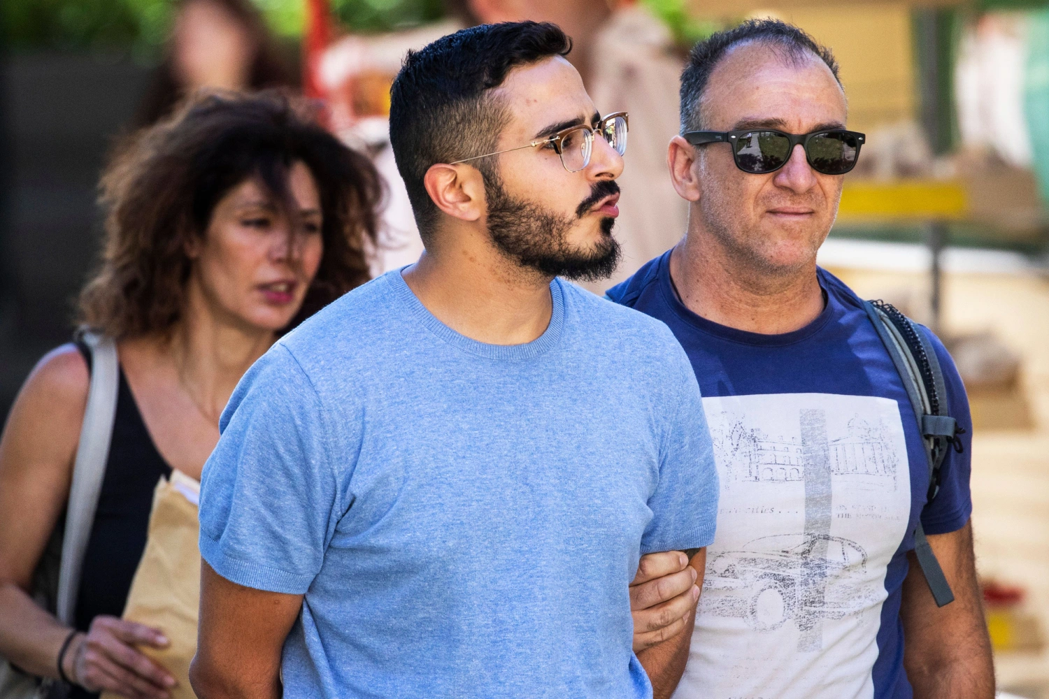 bearded man in blue shirt is led away in handcuffs