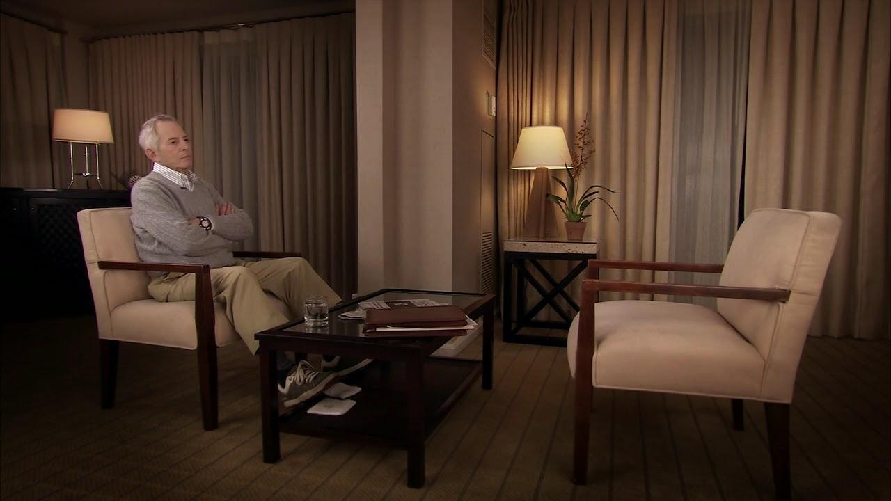 White-haired man with his arms crossed in a hotel room