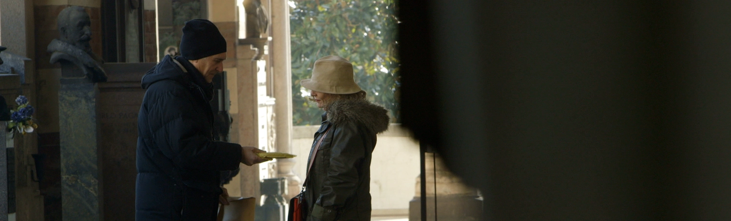 A man wearing a blue balaclava hands an envelope to a long-haired woman.