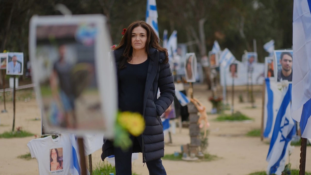 A woman with long, dark hair walks through a field where some victims are remembered.